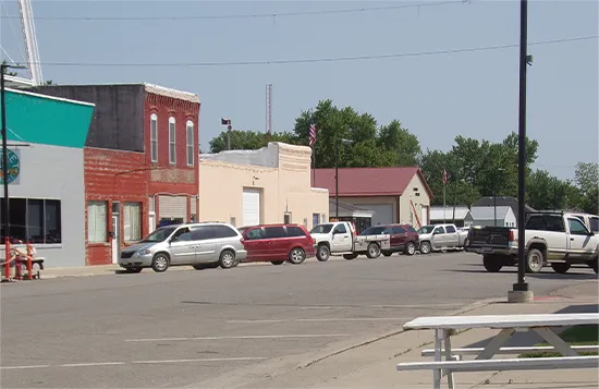 A white bench in Moulton, Iowa Downtown, surrounded by storefronts, cars, and a white picnic table.
